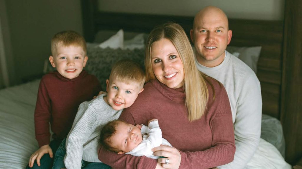 A family is posing for a photo on a bed with Brian Price.